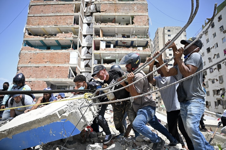 People work together to move a concrete slab with rebar sticking out of it.