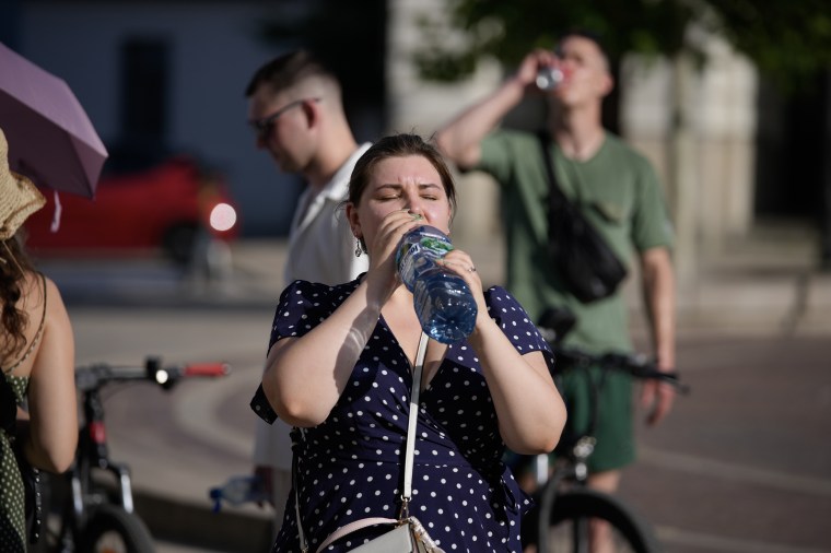 Une femme qui boit de l’eau dans une grande bouteille au soleil ferme les yeux.