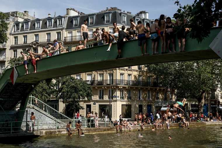 Un groupe de jeunes debout et assis au bord d’un pont au-dessus d’un canal à Paris.