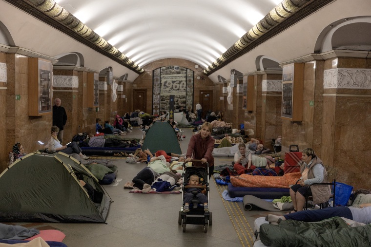 People lying on sleeping bags and inflatable mattresses inside a subway station underground.