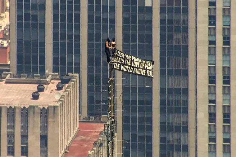 Two people holding a black flag with white lettering on top of the Empire State Building