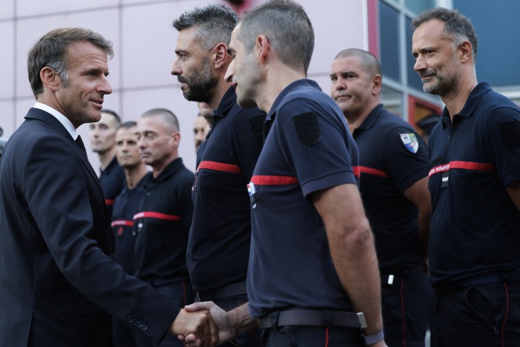 France's President Emmanuel Macron (L) salutes personnel engaged in firefighting efforts.