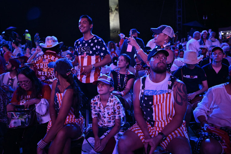 People dressed in red, white and blue attire seated in chairs at night.