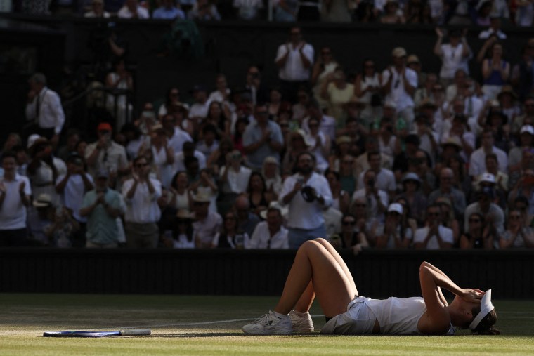 Linda Noskova lying on the grass court at Wimbledon with her hands over her face.