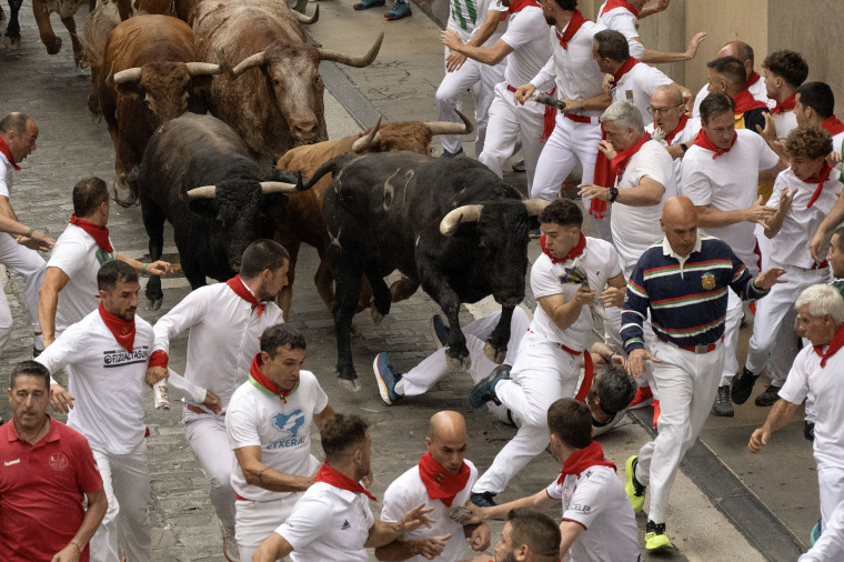 People dressed in white with red neckerchiefs run from bulls on the brick streets of Pamplona.