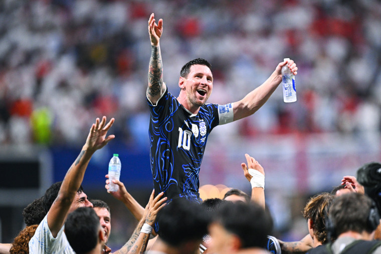 Lionel Messi is carried by his teammates, outstretching his arms in celebration while cheering