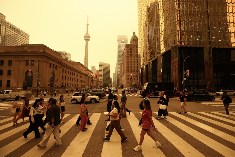 An orange light over a busy downtown scene with pedestrians crossing at an intersection in Toronto.