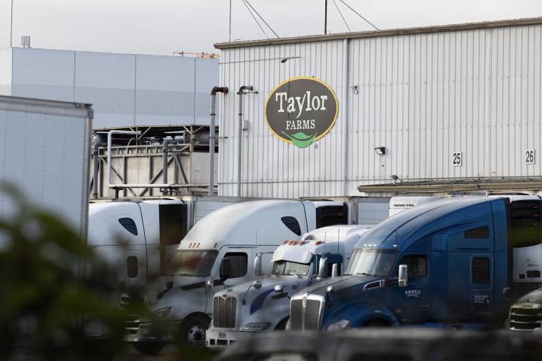 Several semi-trucks parked in front of a warehouse with the Taylor Farms logo on its facade.