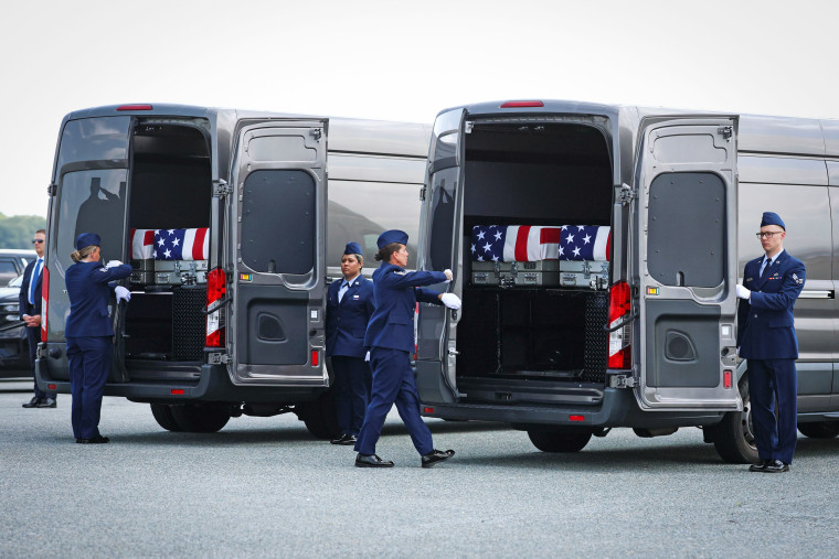 Flag-draped transfer cases are loaded into vehicles during a dignified transfer