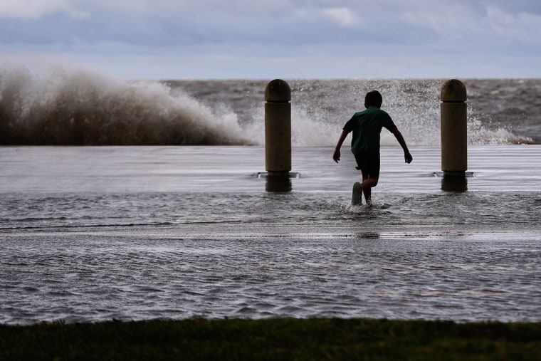 A boy frolics in the water near a lake as a wave crashes