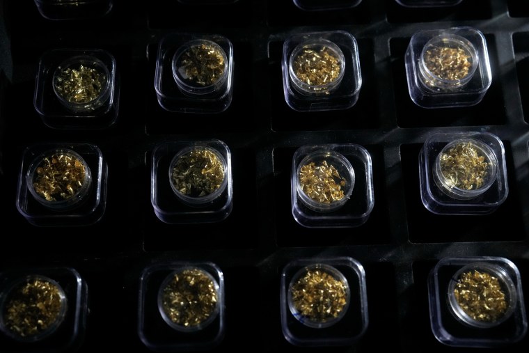 Twelve plastic vials with small pieces of gold in them, lying on a black surface.