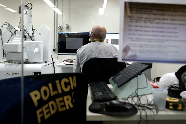 A bald man, seen from behind, sitting at an array of computer monitors.