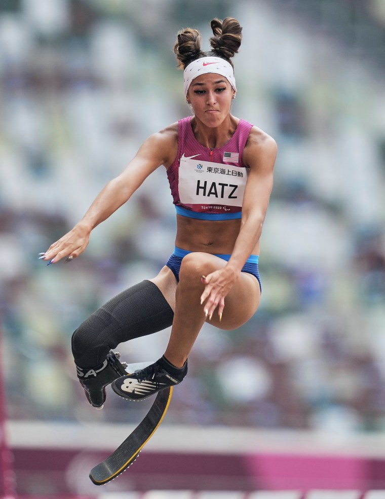 A woman with a prosthetic leg in the air during a long jump event.