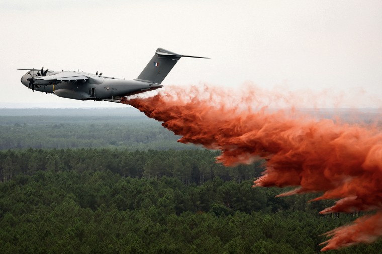 A military plane dropping red fire retardant over thick forest.