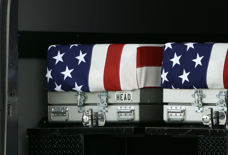 Two metal coffins with American flags draped over them in the back of a cargo truck.