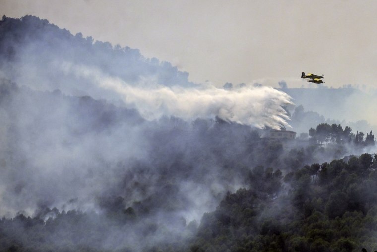 A firefighting aircraft drops water over a wildfire near Betxi, Spain.