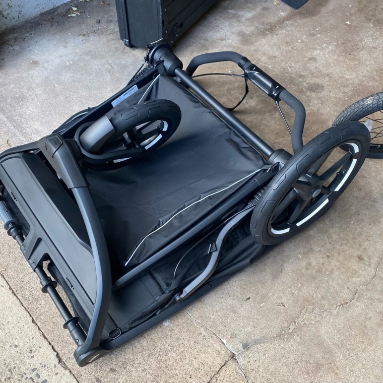 A folded black Thule Urban Glide Double jogging stroller lying on its side on a driveway, showing its large wheels and compact folded frame