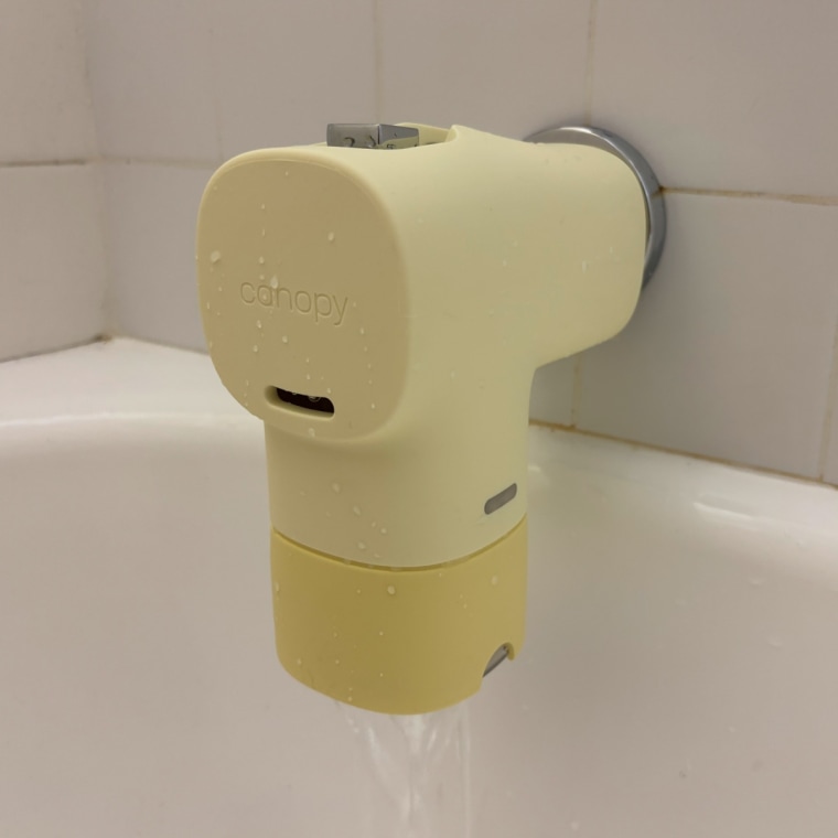 A yellow Canopy Bath Tub Filter installed on a tub spout against a white tile background.