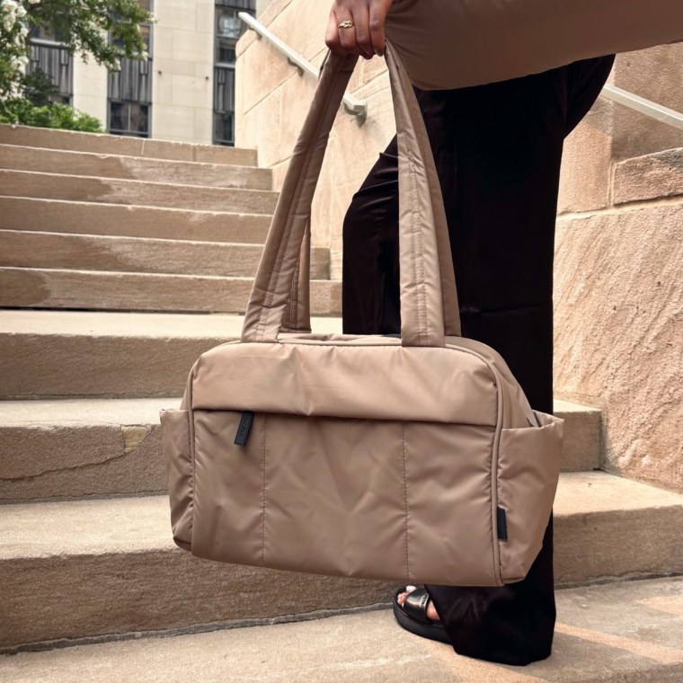 Γυναίκα που κρατά ένα μικρό duffel Luka στο αριστερό χέρι σε μια σκάλα.