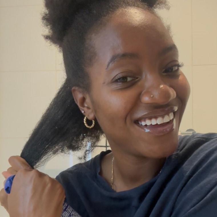 Spraying the Cecred Detangling Spray onto stretched hair while standing in a bathroom.