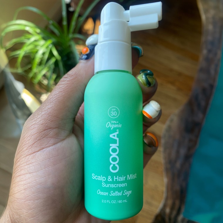 Woman holding bottle of Coola hair and scalp sunscreen