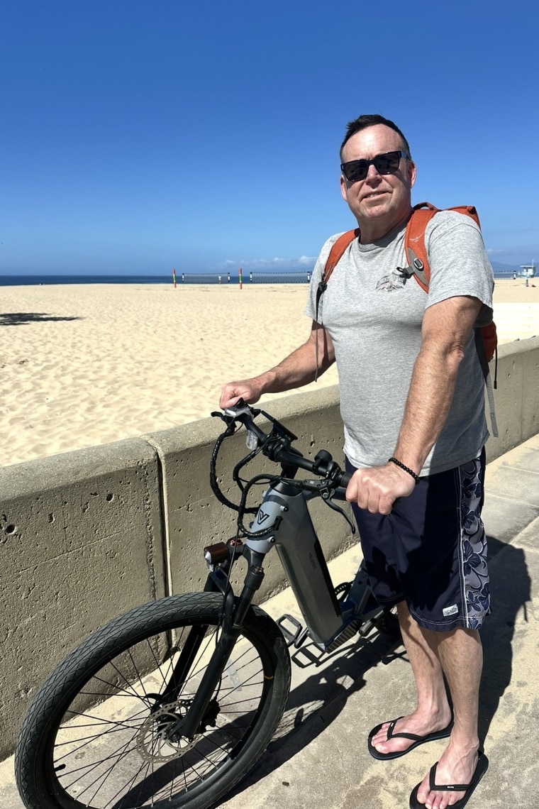 Christopher Claunch posing for a photo on the beach while holding his bike.