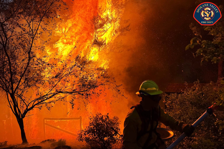 Image: A firefighter facing a large burning wildfire