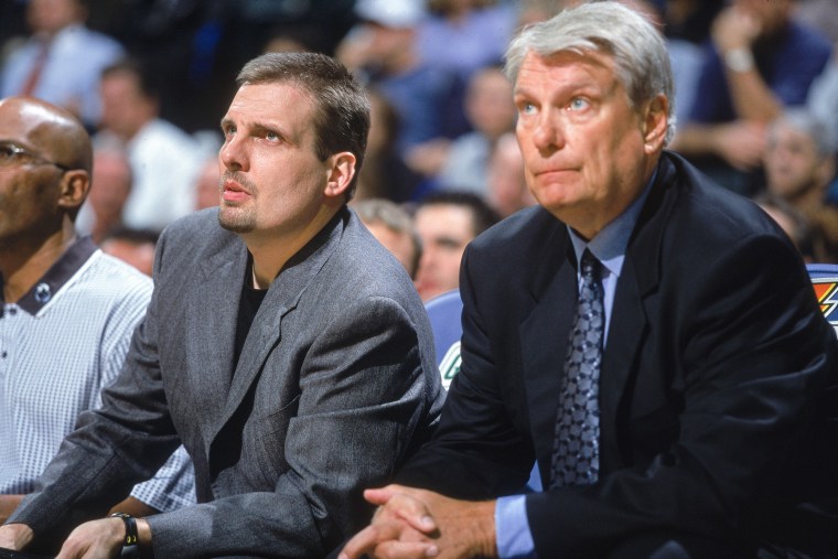 Donnie Nelson, left, and Don Nelson sit side by side on chairs on the side of a basketball court