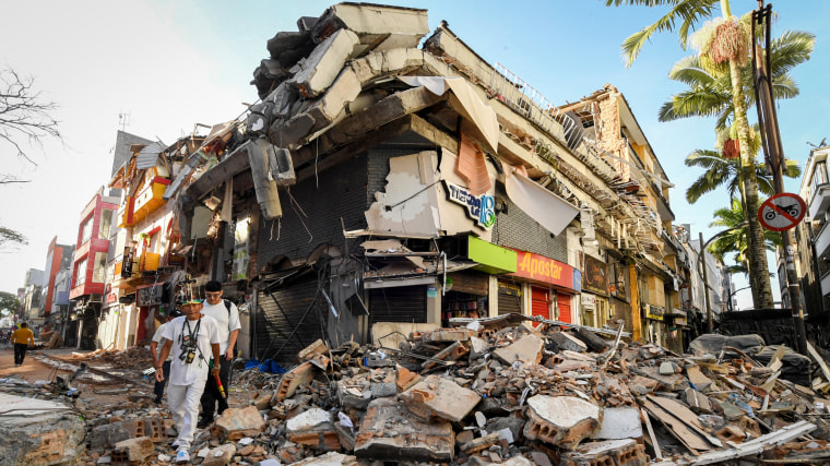 People walk past the rubble of a collapsed building.