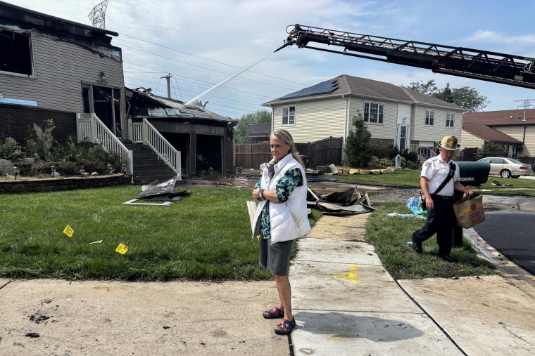A woman stands on a driveway as a fireman walks besides her on a sidewalk.