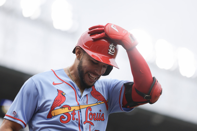 Joshua Báez holds his hand to his batting helmet and smiles.