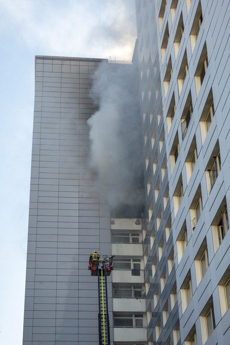 Firefighters on a chairlift next to thick black smoke coming from an apartment's windows.