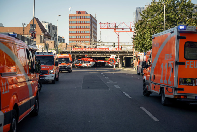 Red emergency vehicles parked in the street, with a helicopter in the background.