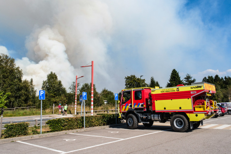 A fire truck parked as a plume of smoke rises into the sky during a wildfire