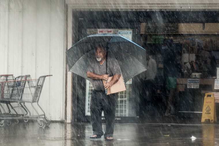 A man with a large umbrella stands in a downpour.