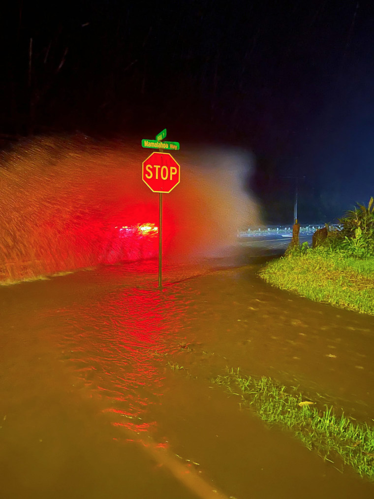 A car drives past a stop sign on a flooded road at night