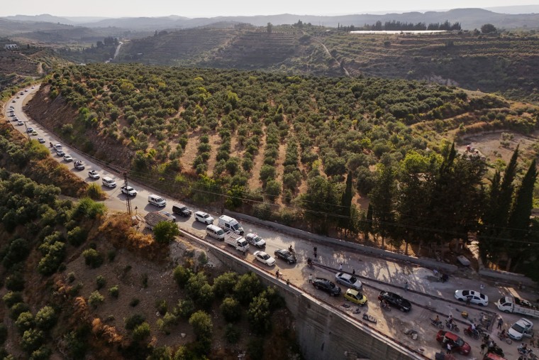 A long line of cars on a highway is seen from above.