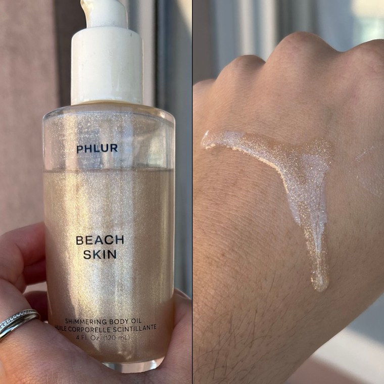 Hand holding the Phlur Beach Skin Shimmering Body Oil bottle in front of a window.