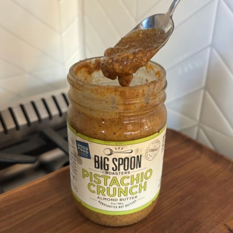 A spoon scooping Big Spoon Roasters’ Pistachio Crunch Almond Butter from the jar.