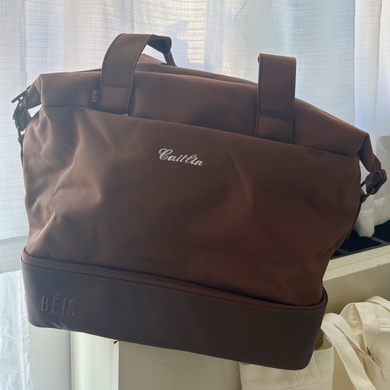 Béis Weekender bag sitting on windowsill in front of white curtains.