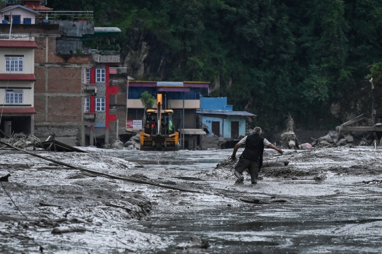 A man walks along a landslide disaster right next to buildings.