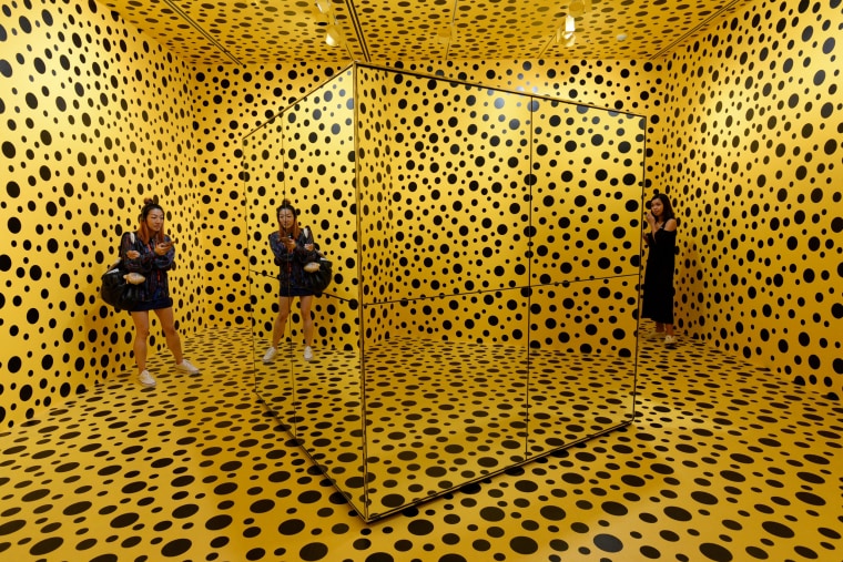 Two women stand inside an art installation by Yayoi Kusuma