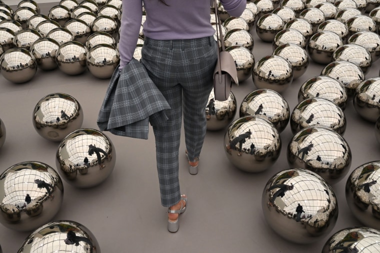 A person walks in an art exhibition displaying spheres on the floor.
