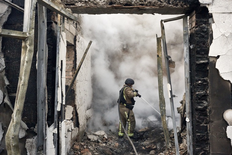 A firefighter spraying a hose into thick smoke in a burning building.