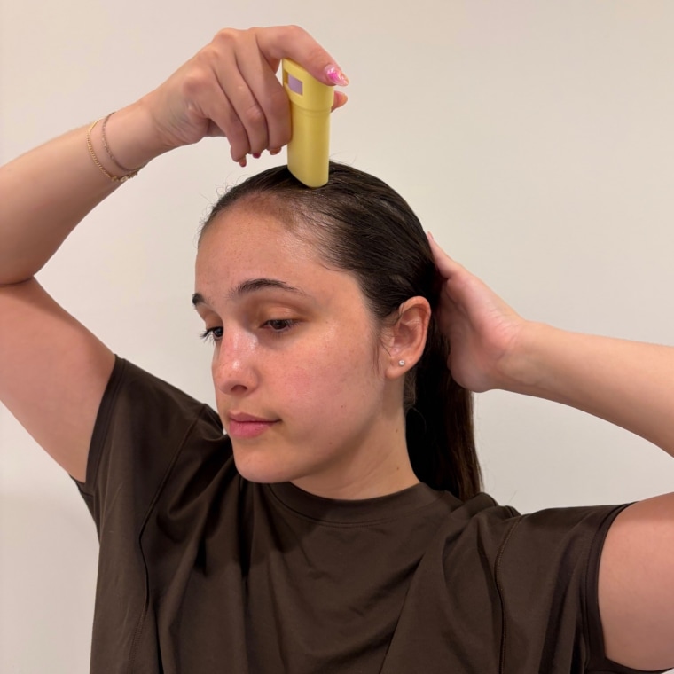 Woman applying JVN wax stick to side of her hair