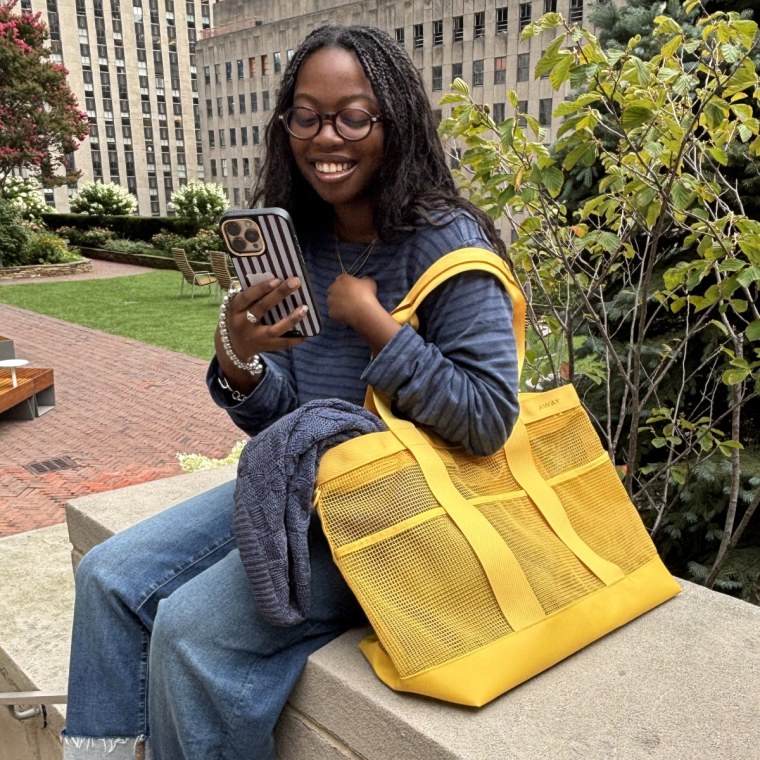 Woman sitting on bench holding a yellow Away Beach Tote and phone.