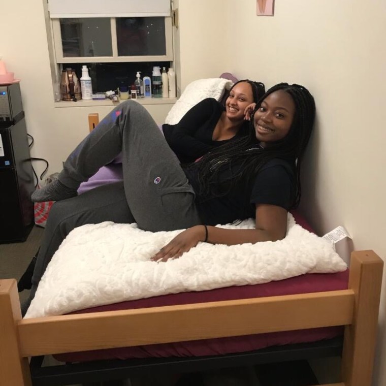 Photo of two girls smiling on a bed in a dorm room