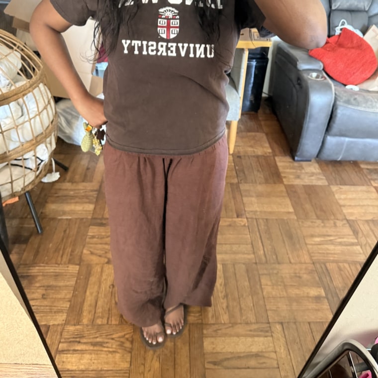 Alabi wearing the Crocs Miami sandals in her living room, with brown pants and a brown tee shirt, photographed in the mirror.