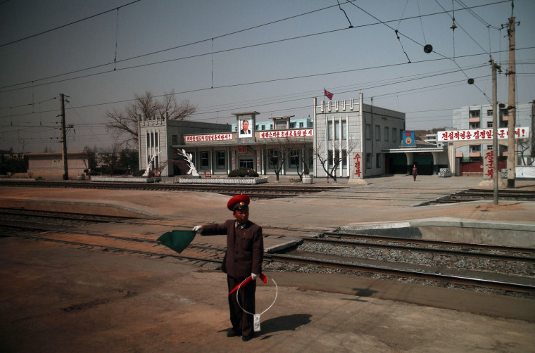 A conductor displays flag signals to a passing-by train outside a station featuring a portrait of North Korean founder Kim Il Sung northwest of Pyongyang, April 8.