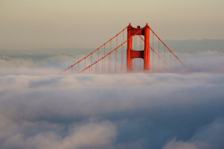 The south tower of the Golden Gate Bridge appears above the evening fog as the suns sets on the Marin Headlands in Sausalito, Calif.